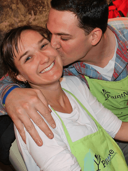 Romantic couple painting together - man kissing woman's cheek during Paint Nite date night